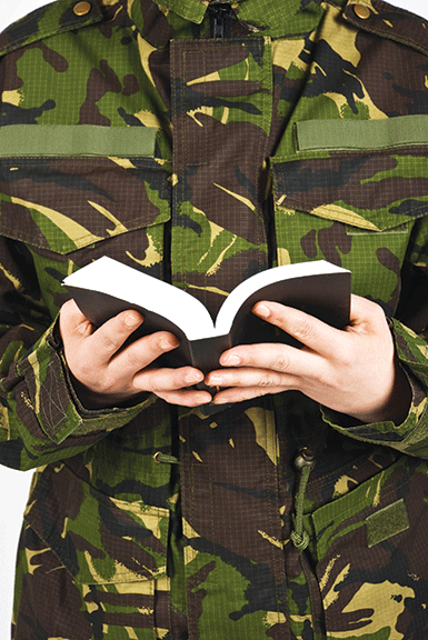Person in camouflage holding an open book, highlighting military and literature themes.