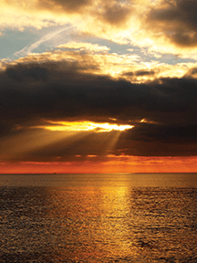 Sunset over the ocean with golden clouds and rays streaming through, creating a serene and picturesque seascape.