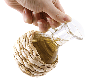 Hand pouring olive oil from woven wrapped glass jug against white background.