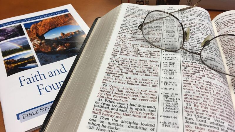 Open Bible with eyeglasses on top, Bible study materials beside, symbolizing faith and learning.