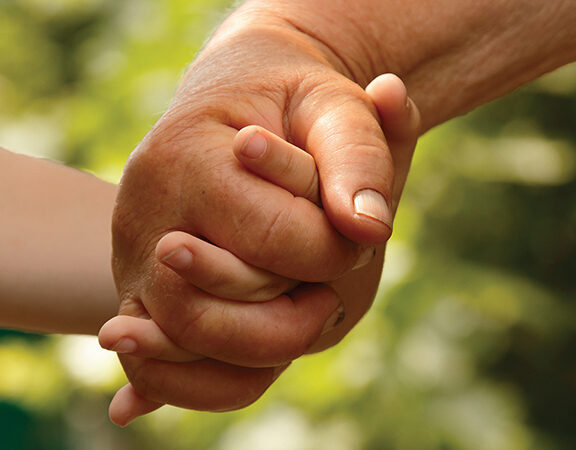 Elderly and young hands holding, symbolizing connection and care against a blurred green background.