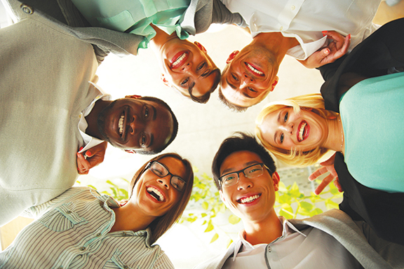 Smiling diverse team in a circle, symbolizing unity and teamwork. View from below with natural light.
