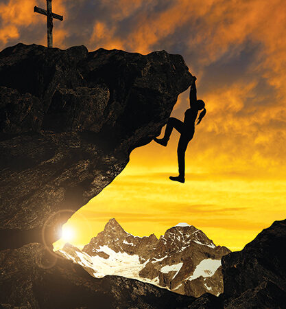 Climber scaling rocky cliff at sunset, cross atop peak, snow-capped mountains in the background.