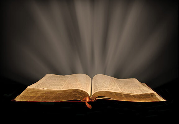 Open book with glowing light rays on a dark background, symbolizing knowledge and inspiration.