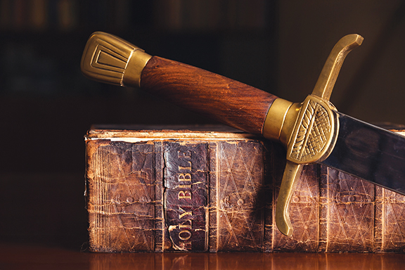 Antique sword rests on an old Bible, symbolizing faith and strength.