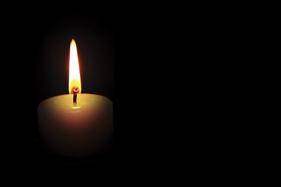 Single lit candle against a dark background, symbolizing hope and light.