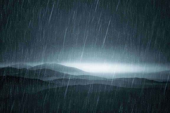 Rainy mountain landscape with layered hills under heavy rain and dark, dramatic sky.