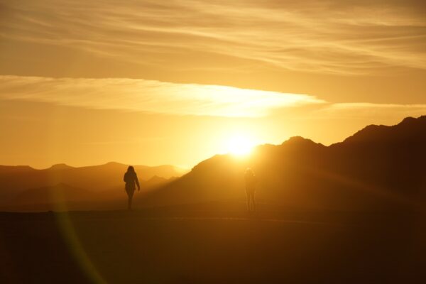 Silhouetted hikers at sunrise on a mountain trail, surrounded by glowing golden light.