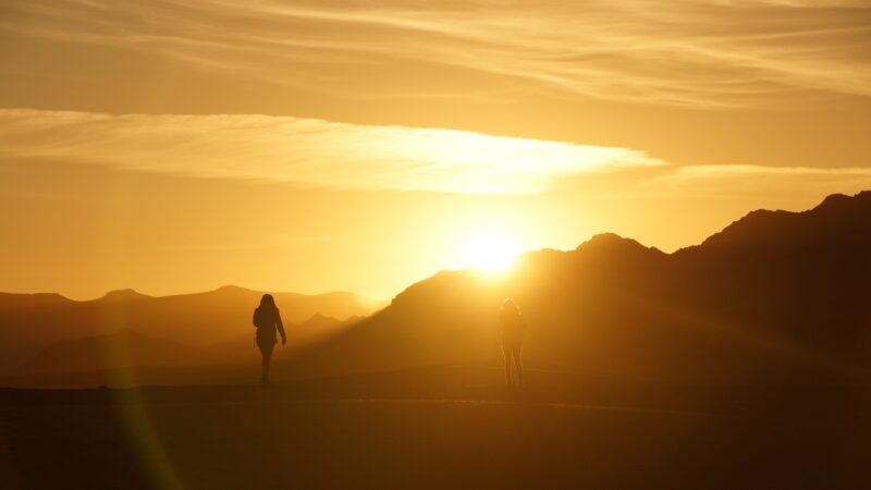 Silhouetted hikers at sunrise on a mountain trail, surrounded by glowing golden light.