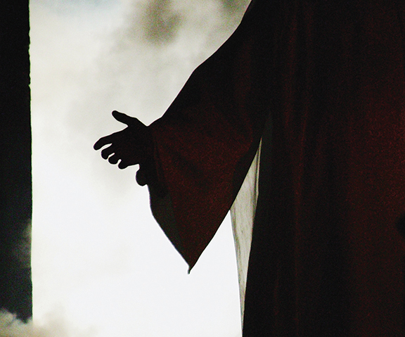 Silhouetted outstretched hand against a bright, cloudy background, evoking a sense of welcome or invitation.