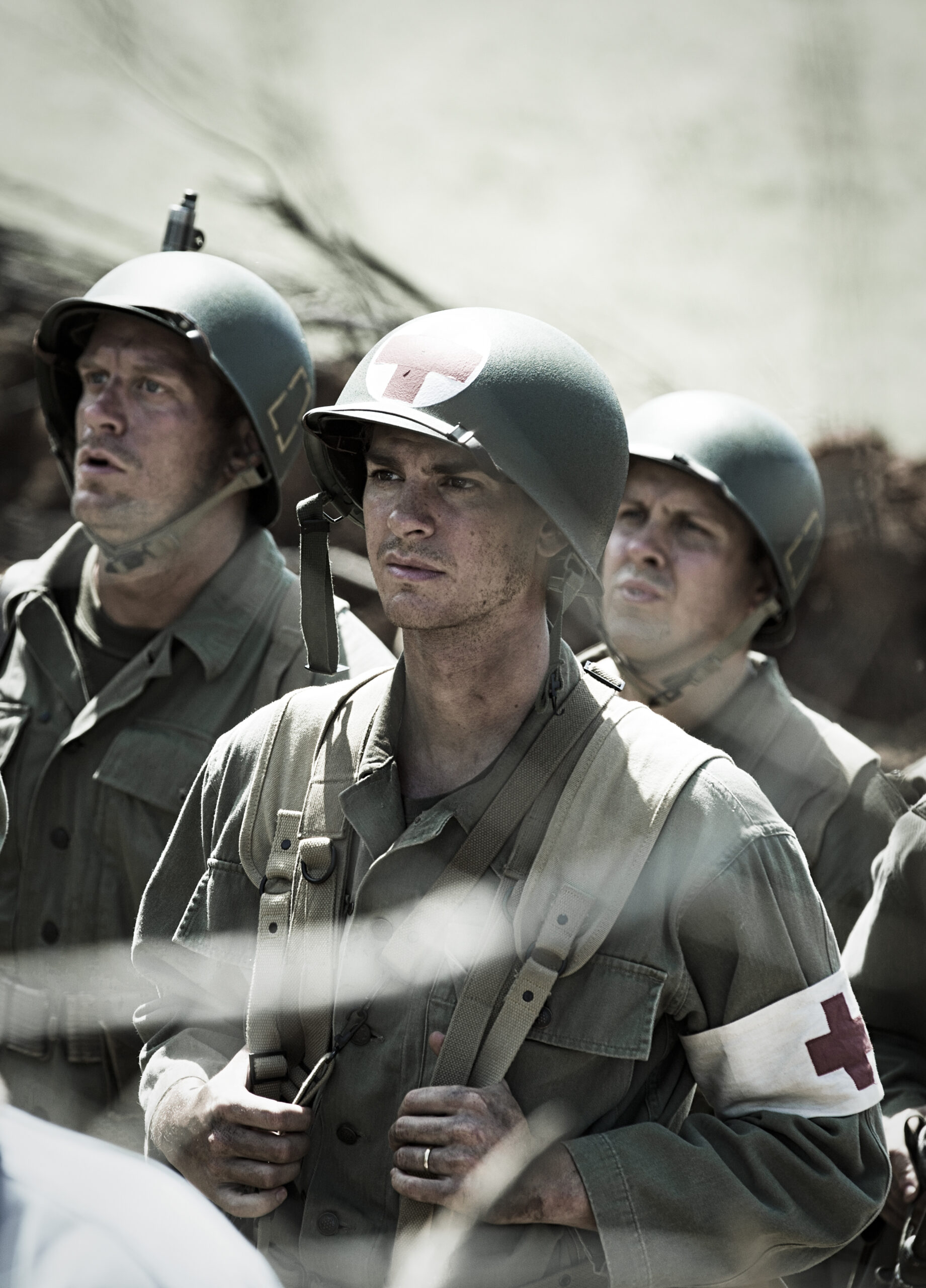Soldiers in World War II uniforms, wearing helmets with medical insignia, stand ready in a battlefield.
