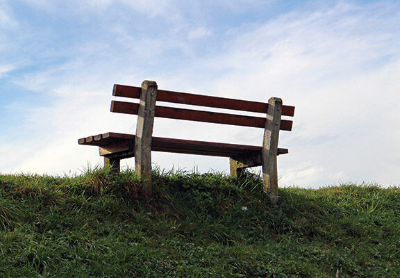Wooden bench on grassy hill under blue sky, ideal for relaxation and nature enjoyment.