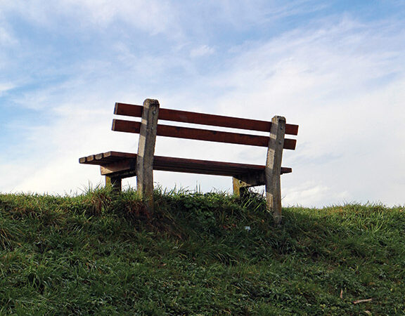 Wooden bench on grassy hill under blue sky, ideal for relaxation and nature enjoyment.