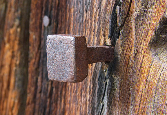 Rustic square nail embedded in textured wood, showcasing vintage carpentry craftsmanship and weathered charm.