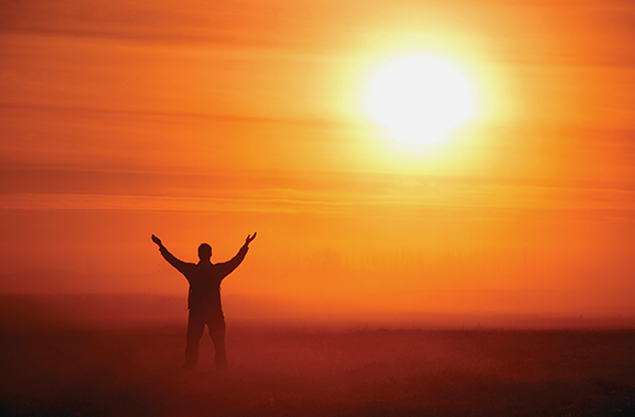Silhouette of person raising arms against vibrant orange sunrise sky for motivation and positivity concept.