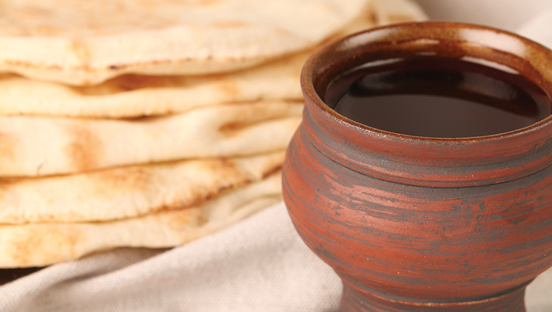 Clay mug of dark beverage beside a stack of flatbread on a beige cloth.