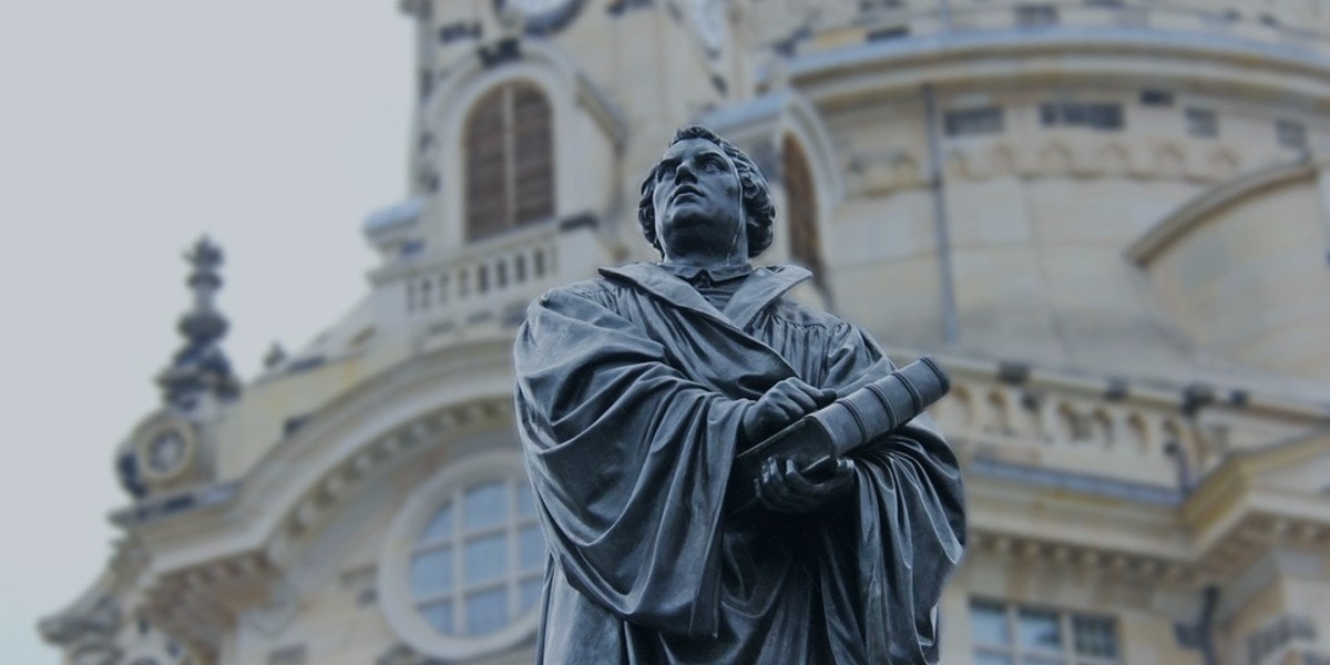 Statue of a historical figure holding a book in front of a detailed architectural building.