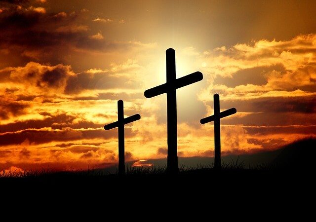 Three crosses silhouetted against a dramatic sunset sky, symbolizing faith and hope.