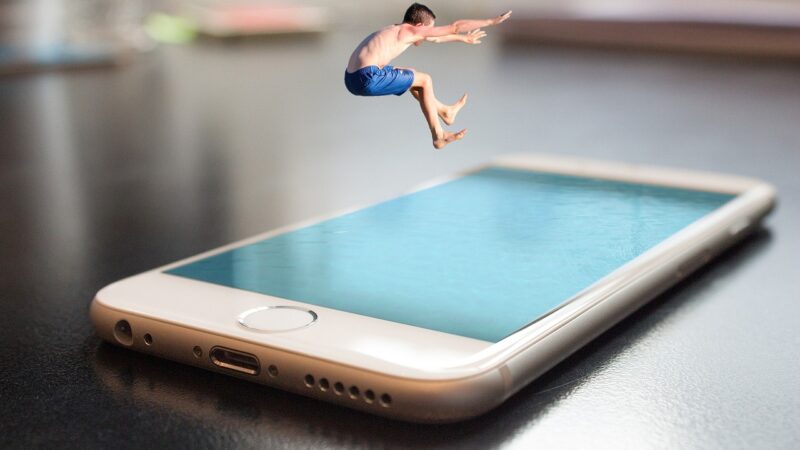 Man in blue shorts jumping into a smartphone pool, symbolizing digital immersion and connectivity.