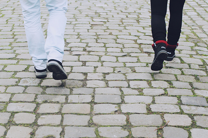 Two people walking on cobblestone street, wearing casual pants and shoes, captured from behind.
