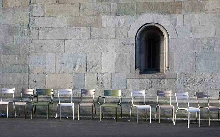 Empty chairs aligned against a stone wall with an arched window.
