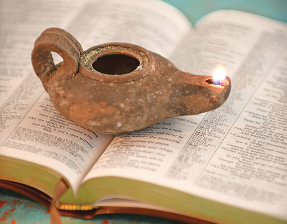 Ancient oil lamp on open Bible, symbolizing spiritual enlightenment and historical reflection.