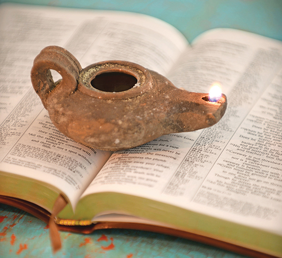 Ancient oil lamp on open Bible, symbolizing spiritual enlightenment and historical reflection.