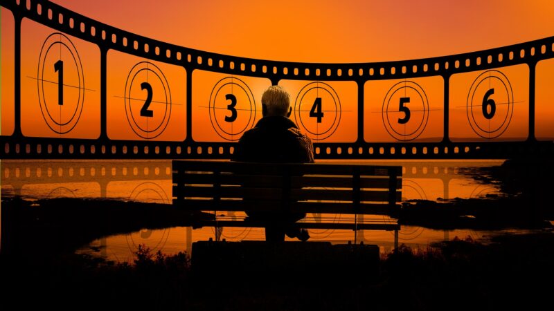 Person sitting on a bench at sunset, film reel countdown overlay, scenic view.