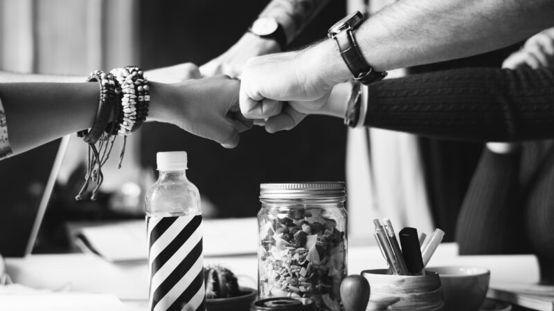 Teamwork success: diverse hands joining in a group fist bump over a table with snacks and a striped bottle.