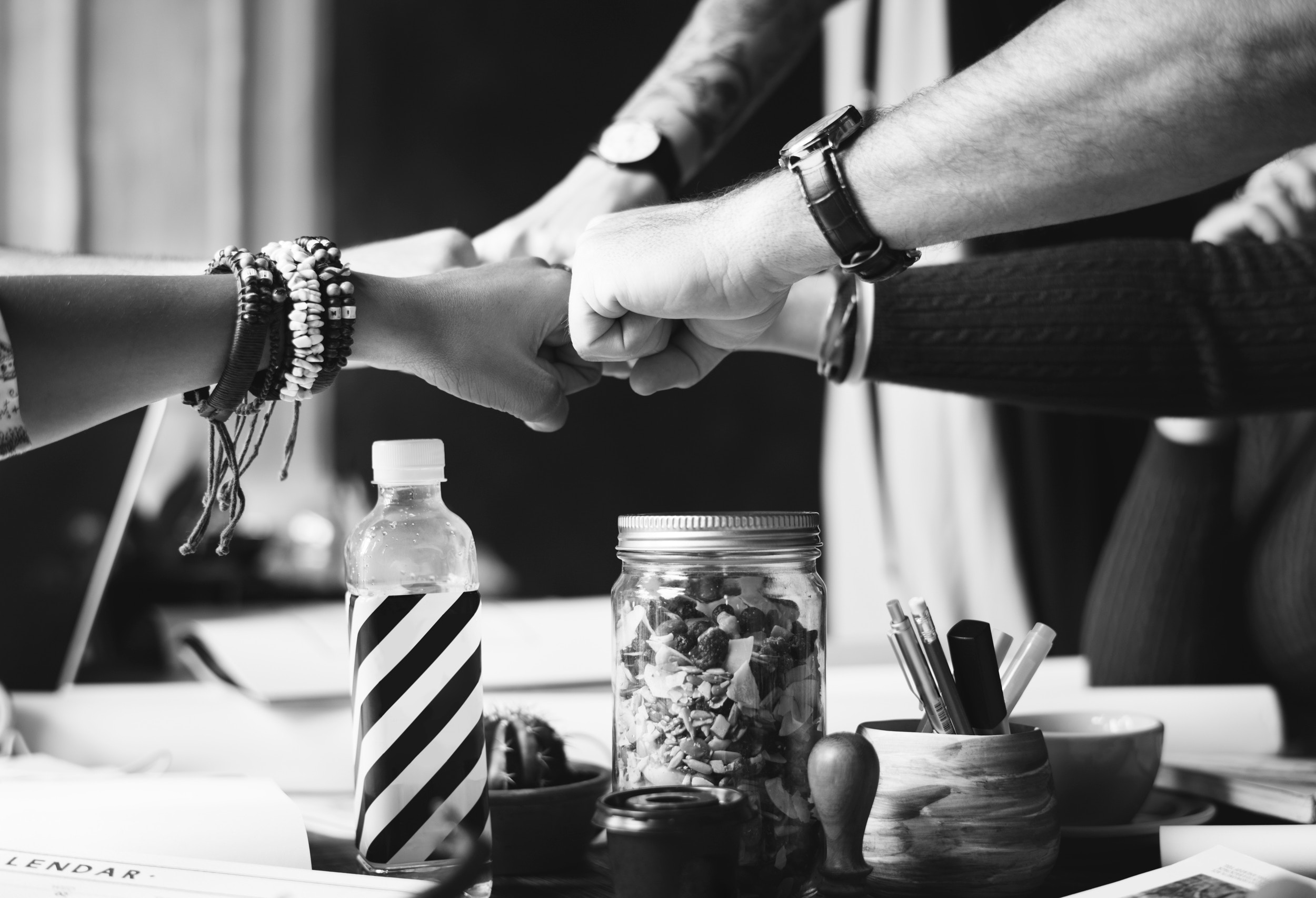 Teamwork success: diverse hands joining in a group fist bump over a table with snacks and a striped bottle.