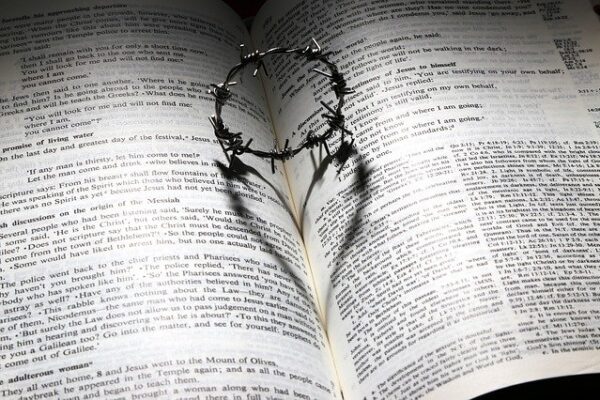 Open Bible with crown of thorns casting heart-shaped shadow, symbolizing love and sacrifice.
