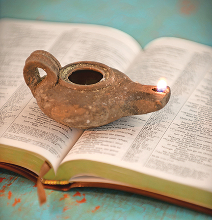 Ancient oil lamp lit on an open book, symbolizing enlightenment and knowledge, with a turquoise background.