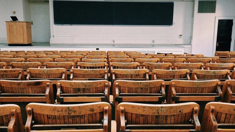 Empty lecture hall with wooden chairs and a blackboard, ready for a university class or seminar.