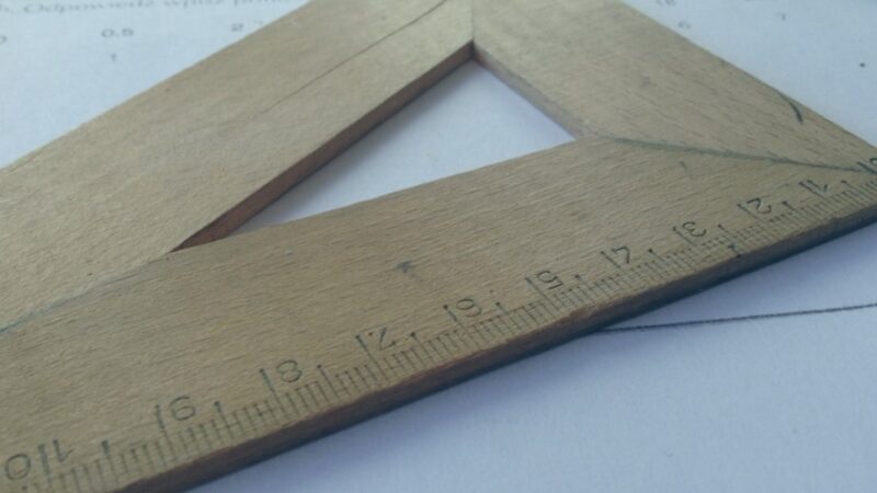 Wooden drafting triangle with metric ruler on paper, essential tool for precision in technical drawing.