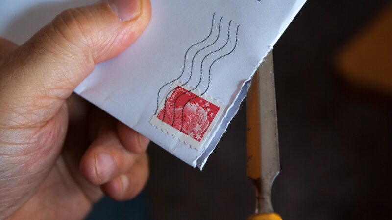 Person opening an envelope with a red postage stamp using a tool for mail processing.