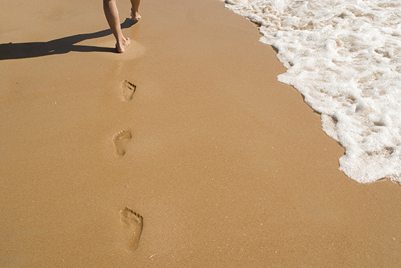 Barefoot prints on sandy beach near ocean waves, representing a peaceful coastal walk.