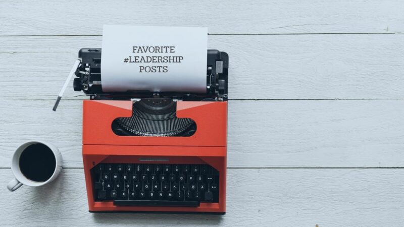 Red typewriter with paper displaying Favorite #Leadership Posts next to a coffee cup on a wooden table.