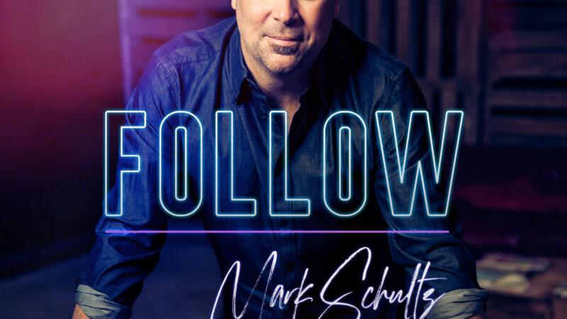 Man in dark shirt, leaning forward, with Follow text overlay. Dimly lit setting, colorful lighting effect.