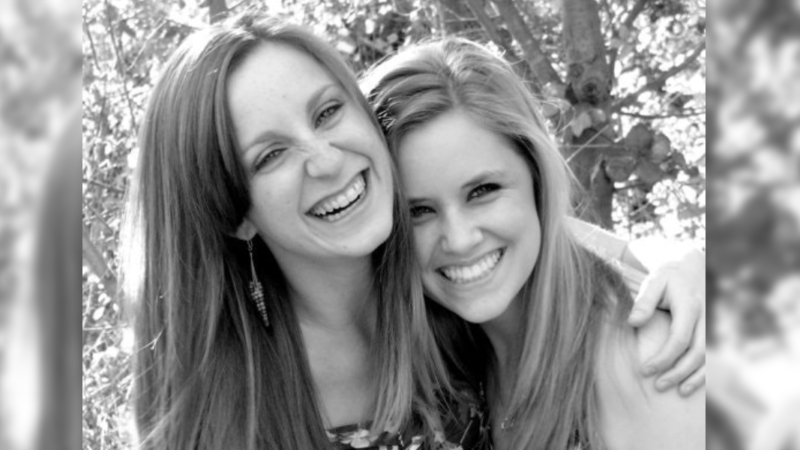 Two women smiling and hugging outdoors on a sunny day, black and white photo, highlighting friendship and joy.