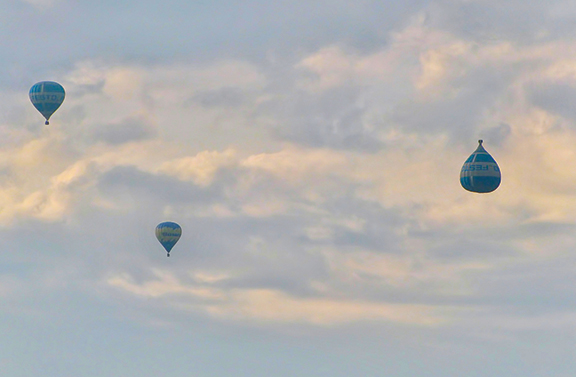 Three hot air balloons floating in a cloudy sky, showcasing a serene and peaceful aerial scene.