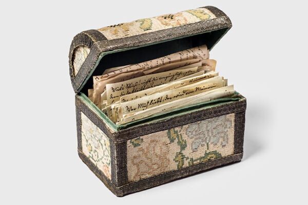Antique box with intricate fabric design, open to reveal historical letters.