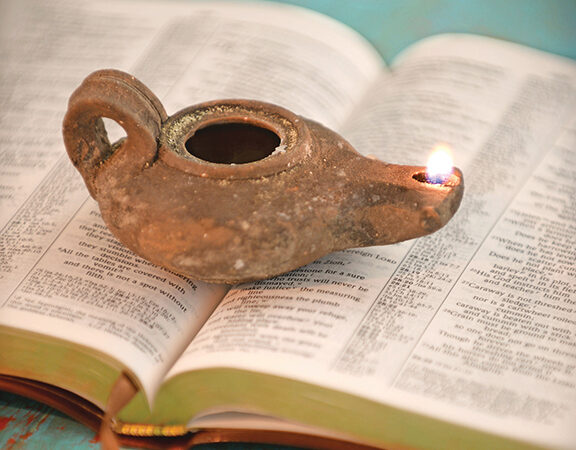 Ancient clay oil lamp burning on an open Bible, symbolizing enlightenment and knowledge.