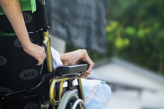 Close-up of a caregiver assisting an elderly person in a wheelchair, outdoors on a sunny day.