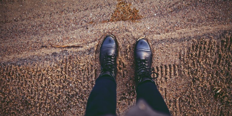 Black boots on sandy beach with visible texture and footprints, person standing on sand.