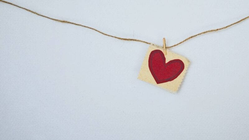 Red heart on fabric card hanging from twine with clothespin, minimalistic love concept.