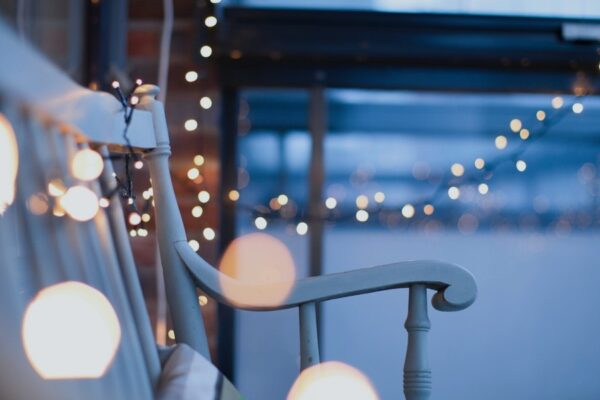 String lights hang around a cozy porch at dusk, creating a warm and inviting ambiance.
