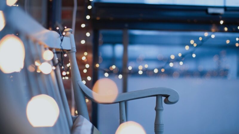 String lights hang around a cozy porch at dusk, creating a warm and inviting ambiance.