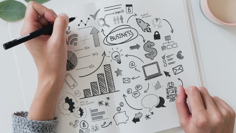 Hand drawing business strategy concepts with graphs, arrows, and icons on white paper.