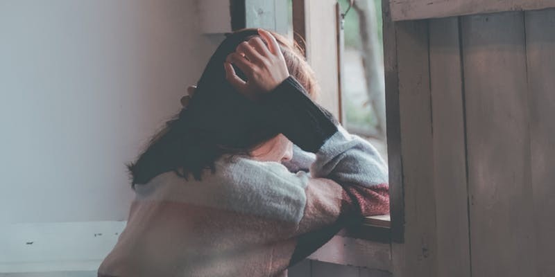 Woman gazing out window wistfully, wearing a colorful sweater, lost in thought. Cozy indoor scene.