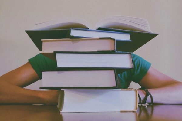 Person overwhelmed by a stack of books, highlighting a challenging study session.